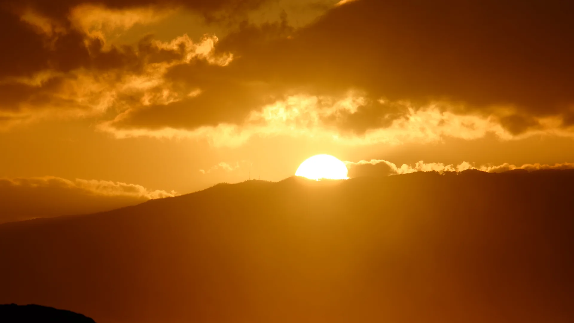 The sun setting behind the silhouetted Waiʻanae Range on Oʻahu's west side, a paddler visible on the water below